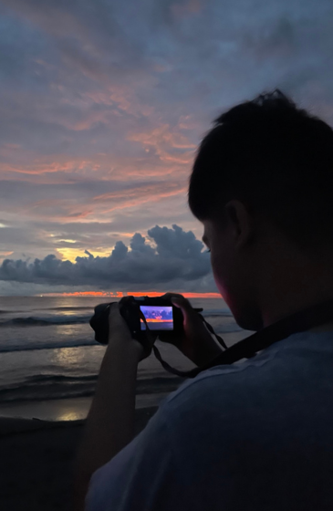 A person holds a camera and photographs a vibrant sunset over the ocean.