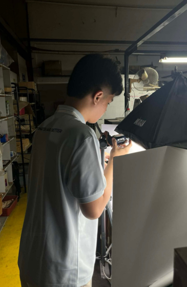 A person in a sky blue shirt works with a camera and tripod in a dimly lit room.
