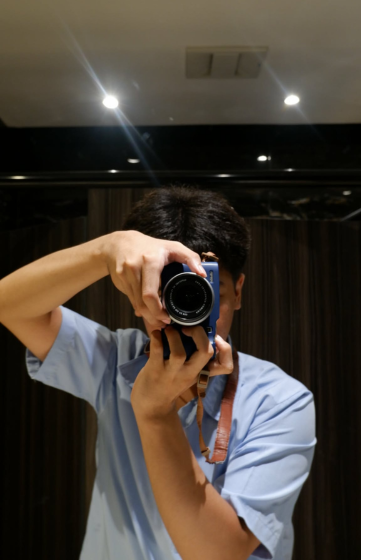 A person in a blue shirt is taking a selfie in a mirror with a camera.