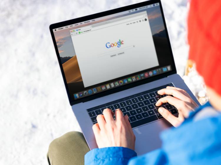 Person in a blue jacket using a laptop outdoors in snow.